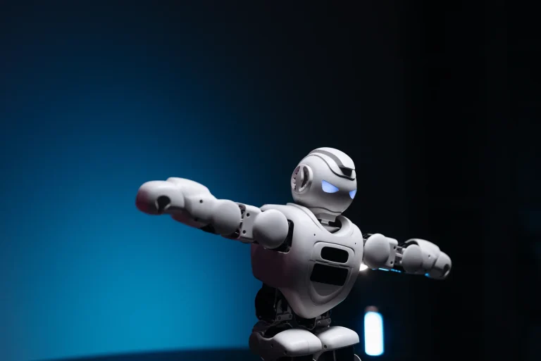 Biały robot humanoidalny ze świecącymi na niebiesko oczami rozkłada ramiona na ciemnym, granatowym tle