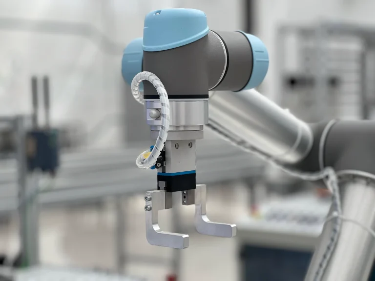 Ramię robota współpracującego z dwupalczastym chwytakiem na hali produkcyjnej, w chłodnym szaro-błękitnym świetle